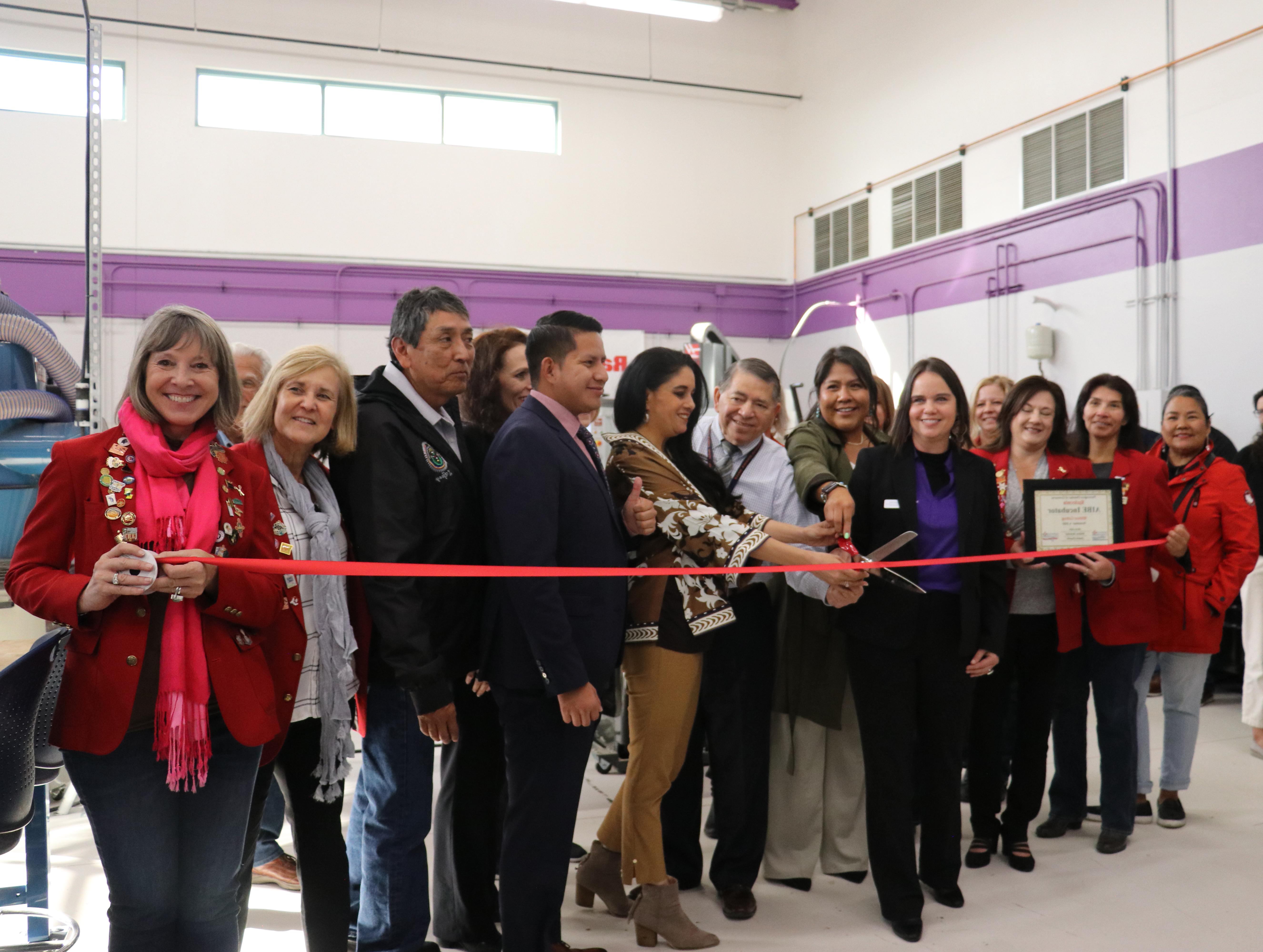 Group of people prepare for a red ribbon cutting.