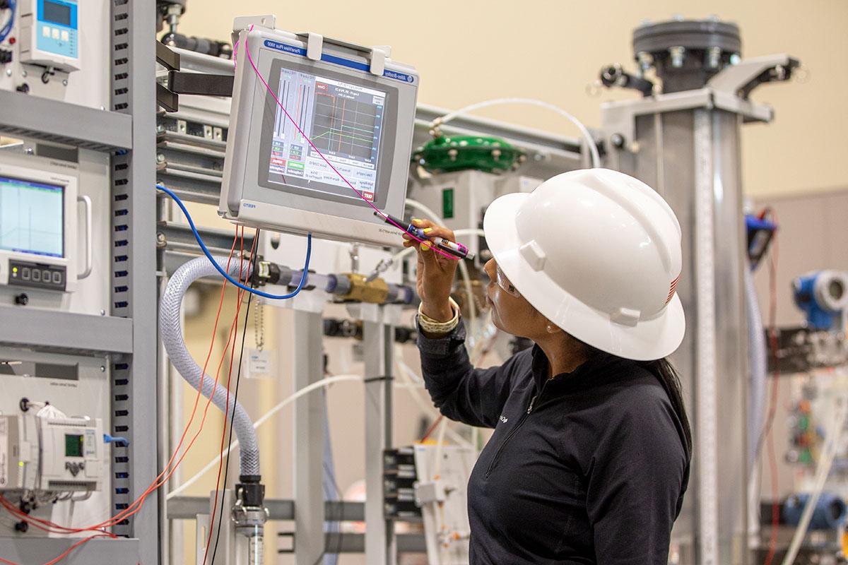 A person in a white hard hat looks at a monitor with various machines in the background